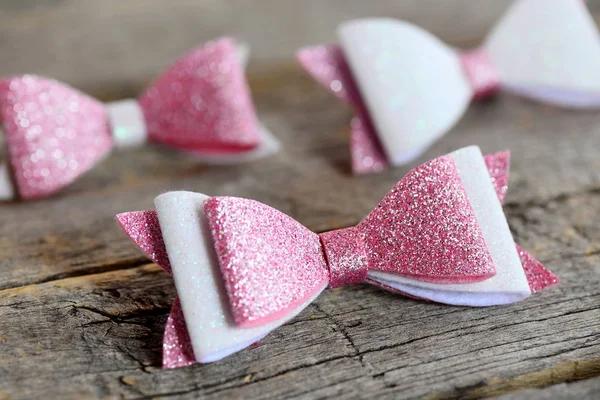 Nice hair bows accessories made of light pink and white felt with sequins. Hair bows for girls on an old wooden table. Closeup