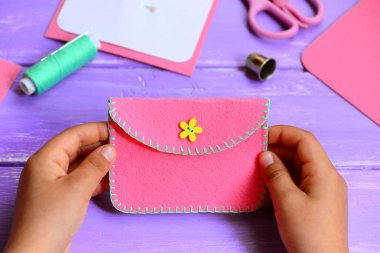 Çocuk bir Keçe Çanta yaptım. Küçük çocuk bir Pembe Keçe Çanta elinde tutar. Tekne üzerinde ahşap bir tablo sağlar. Çocuklar için eğlenceli ve kolay dikiş proje