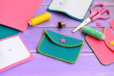 Sevimli yeşil ve Pembe Keçe Çantalar ile çiçek ahşap düğme. Makas, Tel, iğne, yüksük, ahşap bir masa üzerinde kağıt şablonları. El dikiş Atölyesi kavramı