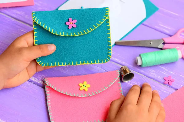 A criança coseu uma bolsa de feltro. A criança pequena segura uma bolsa de feltro brilhante em suas mãos. Artesanato suprimentos, senti diy em uma mesa de madeira. Projeto de costura engraçado e simples para crianças — Fotografia de Stock