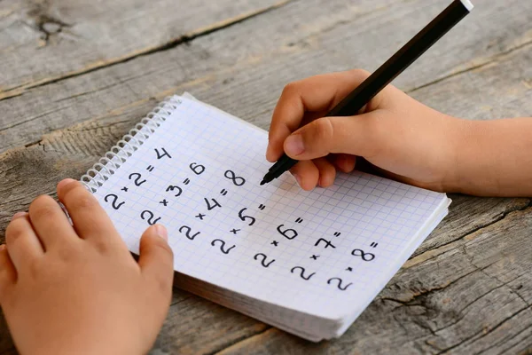 El estudiante de matemáticas resuelve ejemplos de multiplicación. Niño tiene un marcador negro en la mano y escribe respuestas matemáticas. Cuaderno con ejemplos de tabla de multiplicación. Enseñanza de tabla de multiplicación. Niños haciendo matemáticas — Foto de Stock