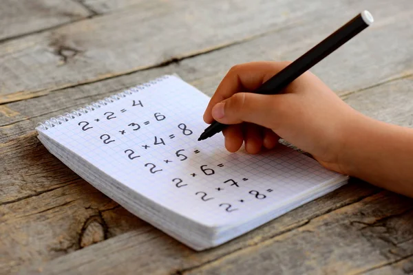 Dziecko rozwiązuje przykłady matematyczne. Dziecko trzyma czarny marker w ręku. Zeszyt z przykładami tabel mnożenia. Badam koncepcję tablicy mnożenia. Praca z liczbami. Dziewczyna robi matmę. — Zdjęcie stockowe