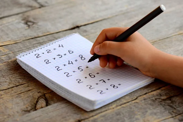 Child resuelve ejemplos matemáticos. El niño tiene un marcador negro en la mano. Hoja de cuaderno con ejemplos de tabla de multiplicación. Estudiar un concepto de tabla de multiplicación. Trabajando con números. Chica haciendo matemáticas — Foto de Stock