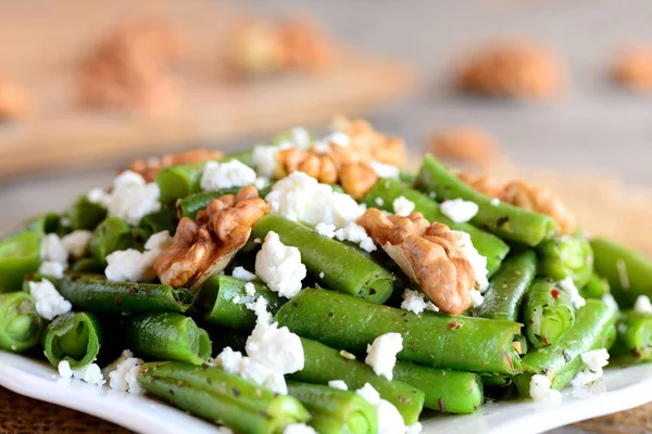 Homemade warm green beans salad. Green bean salad with cottage cheese, raw shelled walnuts, garlic and spices on a plate and an old wooden table. Closeup