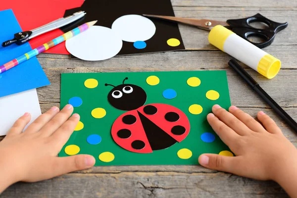 stock image Small child shows a ladybird card. Child made a card with ladybird. Stationery set on a desk. Preschool paper project. Developing children fine motor skills