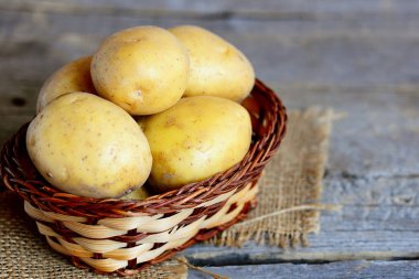Taze patates hasat. Bir çuval bezi ve vintage ahşap arka plan üzerinde bir hasır sepet içinde taze sarı patates. Portre