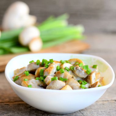 Fried dilimleri ekşi krema ve bir kase içinde genç yeşil soğan ile mantar. Ev yapımı mantar yemek. Antika ahşap masa. Rustik tarzı. Portre