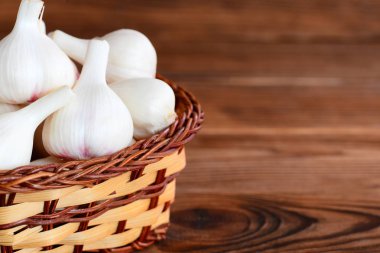 Çiğ beyaz sarımsak bir hasır sepet ve boş metin için bir kahverengi ahşap zemin üzerine. Doğal genç sarımsak ampuller kavramı hasat. Portre