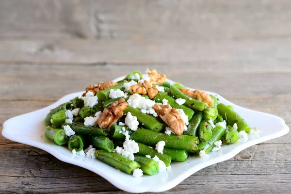 Green string beans with homemade cottage cheese and walnuts on a white plate and vintage wood background. Closeup