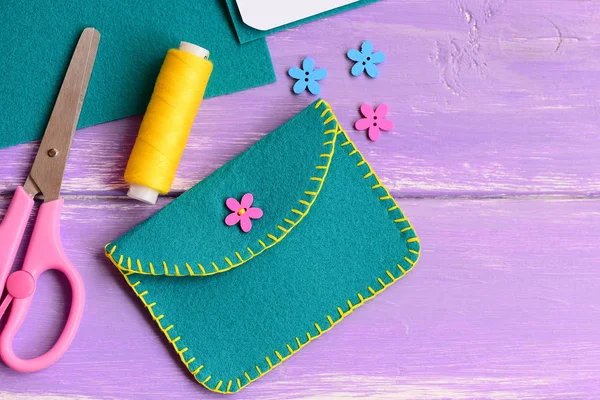 Bolsa de feltro pequena com botão de madeira flor. Tesoura, linha, flor botão de madeira em um fundo de madeira com espaço de cópia para texto. Costura de mão para crianças — Fotografia de Stock