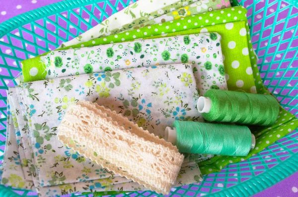 Green fabric, lace and thread in a green box on purple background