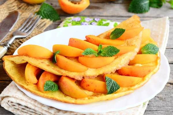 Doce omelete de damasco. omelete recheado com damascos frescos em uma placa branca e um velho fundo de madeira. Receita de café da manhã fácil verão. Fechar. — Fotografia de Stock