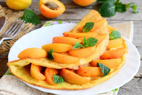 Abrikoos omelet recept. Omelet gevuld met verse abrikozen plakjes en versierd met muntblaadjes op een witte plaat en een vintage houten tafel. Creatieve gezond ontbijt idee. Closeup — Stockfoto