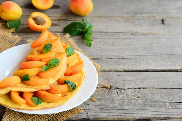 Zomer abrikoos omelet. Omelet gevuld met verse abrikozen plakjes en muntblaadjes op een witte plaat en een vintage houten achtergrond met lege ruimte voor tekst. Mooie ontbijt idee — Stockfoto