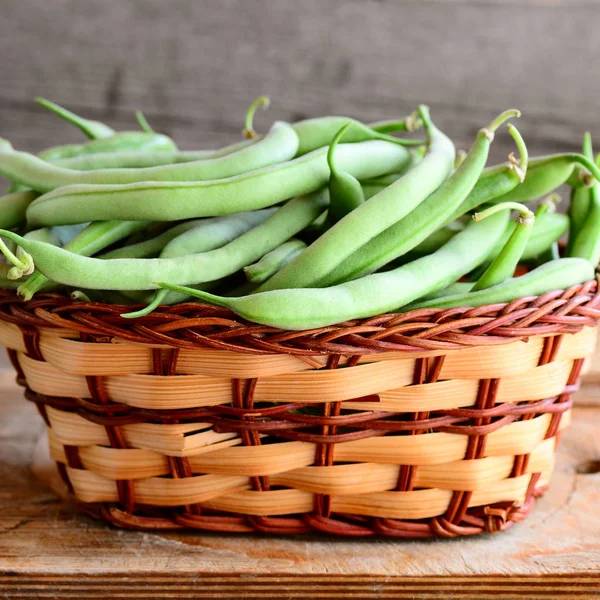 Grüne Saitenbohnen in einem Weidenkorb und einem Holzbrett. rohe junge Bohnen Schoten. alten hölzernen Hintergrund. saisonales Erntekonzept. Nahaufnahme — Stockfoto