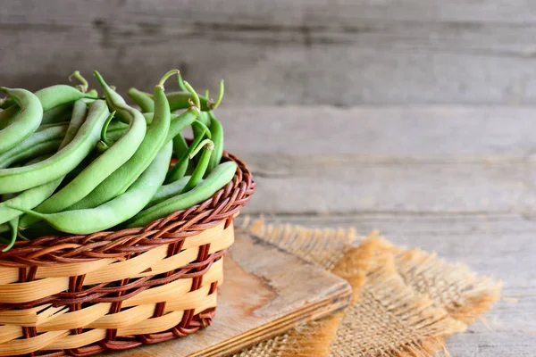 Grüne Saitenbohnen in einem Weidenkorb und einer Platte. natürliche unreife Bohnen Schoten. rustikaler Holzhintergrund mit Kopierraum für Text. Konzept zur Ernte grüner Stringbohnen — Stockfoto