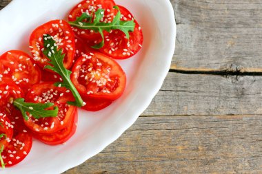 Domates ve Roka Salatası. Ev yapımı taze domates, roka ve Susam salata beyaz plaka ve vintage ahşap arka plan kopya alanı metin için 