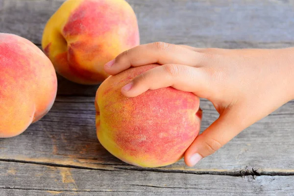 Klein kind neemt een rijpe perzik. Zoete verse perziken op een vintage houten tafel. Heerlijke en gezonde voeding voor kinderen in de zomer — Stockfoto