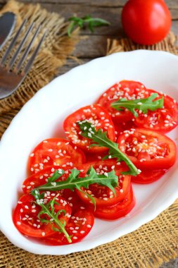 Taze domates, rucola ve susam tohumu salata. Beyaz bir levha ve çuval bezi Tekstil üzerinde yaz sebze salatası. Dikey fotoğraf