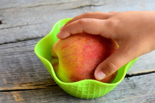 Un niño pequeño toma un melocotón fresco en su mano. Melocotones jugosos dulces en una mesa de madera vintage. Alimentos naturales para apoyar el crecimiento saludable y el desarrollo del niño — Foto de Stock