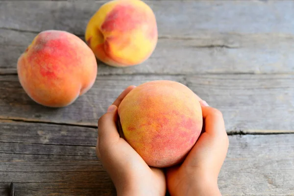 Ein kleines Kind hält einen reifen Pfirsich in den Händen. süße köstliche Pfirsiche auf einem alten Holztisch. Förderung gesunder Ernährungsgewohnheiten für Kinder — Stockfoto