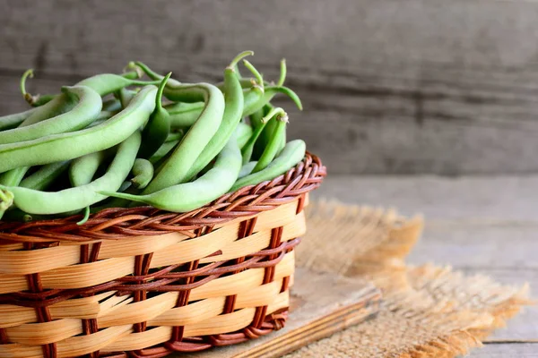 Haricots verts frais dans un panier en osier et sur une planche en bois. Haricots verts non mûrs, source biologique de fibres alimentaires, vitamines et minéraux. Fond en bois — Photo