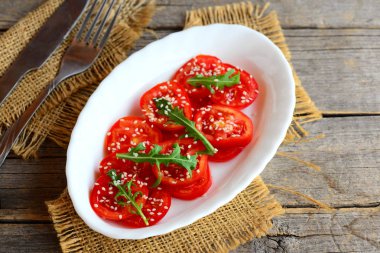 Işık domates, roka ve susam tohumu salatası. Ev yapımı diyet salata beyaz plaka ve çuval bezi peçeteye. Çatal ve bıçak bir vintage ahşap tablo