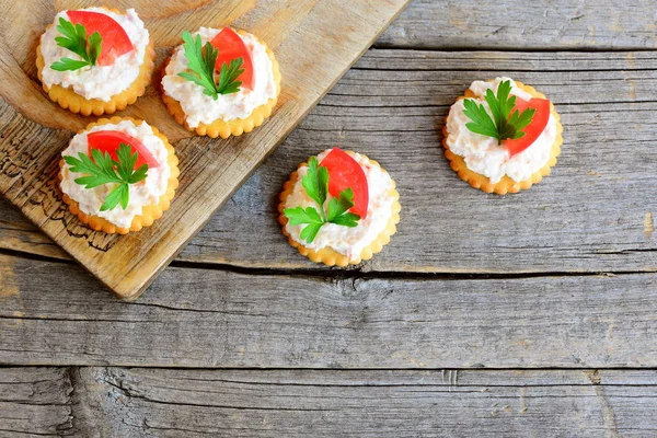 Baharatlı peynir, domates dilim ve yeşil maydanoz yaprağı ile tuzlu kraker üzerinden kanepe pişmiş. Baharatlı peynir kanepe eski bir ahşap zemin üzerinde. Hızlı aperatif tarifi. Üstten Görünüm