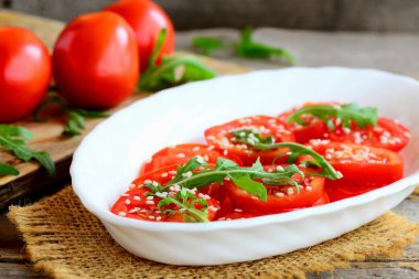 Ripe domates dilimleri, roka roket ve susam tohumu salatası. Beyaz bir levha ve çuval bezi Tekstil üzerinde Bahçe domates salatası. Diyet öğle veya akşam yemeği fikir. Portre