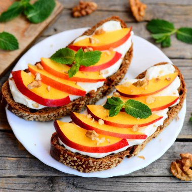 Tatlı kuru soğan, ceviz ve krem peynirli sandviç. Çavdar ekmeği açık sandviçle krem peynir, olgun nektarin, ceviz ve nane bir beyaz plaka ve ahşap masa. Yaz tatlı tarifi. Portre