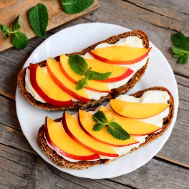 Plaka ve vintage ahşap arka plan üzerinde kuru soğan krem peynirli sandviç. Açık sandviçler çavdar ekmeği, taze nektarin ve yumuşak peynir krem pişmiş. Portre