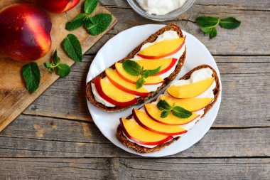 Plaka ve vintage ahşap bir masa üzerinde kuru soğan krem peynirli sandviç. Çavdar ekmeği sandviç taze nektarin ve yumuşak peynir krema ile. Üstten Görünüm