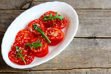 Salata taze domates, rucola, susam ve izole kopya alanı eski bir ahşap zemin üzerine beyaz bir tabak salata sosu ile. Sağlıklı yemek Kahvaltı, öğle ve akşam yemeği için. Rustik tarzı