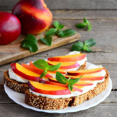 Yumuşak peynir, taze nektarin dilimleri ve nane ile kahvaltı sandviç. Sağlıklı protein sandviç bir tabak ve vintage ahşap masa. Rustik tarzı. Portre