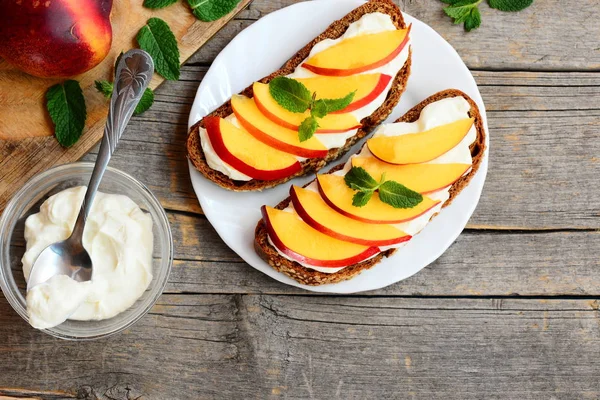 Yumuşak peynir ve taze nektarin dilimleri ile basit çavdar sandviç. Bir plaka üzerinde parlak yaz sandviç. Ahşap antika arka plan kopya alanı ile. Üstten Görünüm 