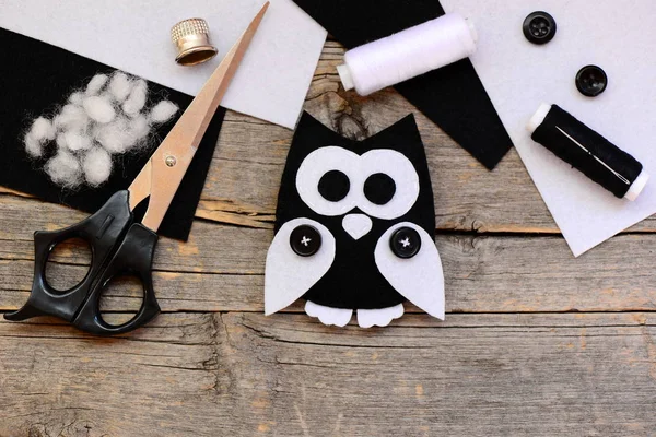 Black and white felt owl, felt sheets, scissors, threads, thimble, buttons on a vintage wooden table. Creating pretty owl ornament from felt. Felt craft used in kids handicraft. Top view — Stock Photo, Image