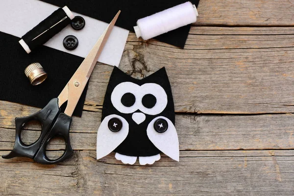 Stuffed felt owl toy, black and white felt sheets, scissors, threads, buttons on a vintage wooden background with copy space. Creating adorable owl toy from felt. Owl crafts idea for kids. Top view — Stock Photo, Image