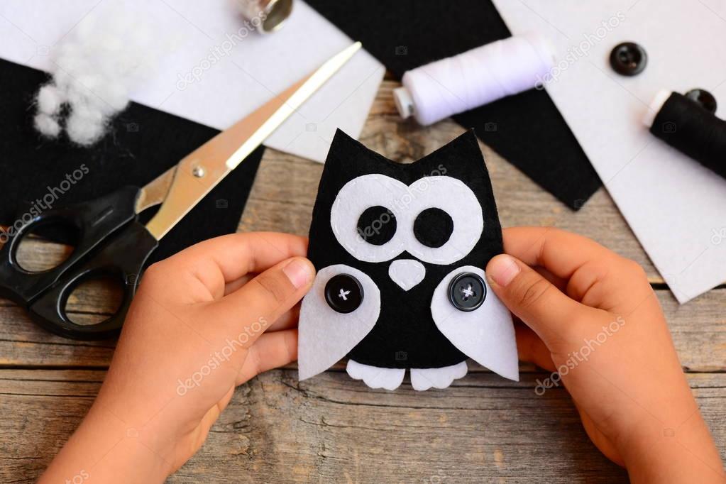 Child holds a felt owl toy in his hand. Small child made an owl out of black and white felt. Teaching children simple sewing skills at home. Sewing concept 