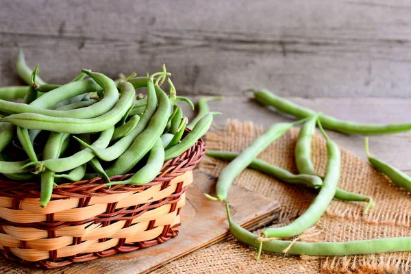 Lange grüne Bohnen in einem braunen Weidenkorb auf einem Holzbrett und einem Klebetuch. hölzerner Hintergrund — Stockfoto