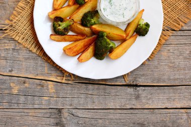 Basit kavrulmuş patates ve brokoli ile dereotu ekşi krema bir plaka üzerinde ve ahşap arka plan metin için boş yer ile. Kavrulmuş patates dilimleri ve brokoli tarifi fikir. Üstten Görünüm