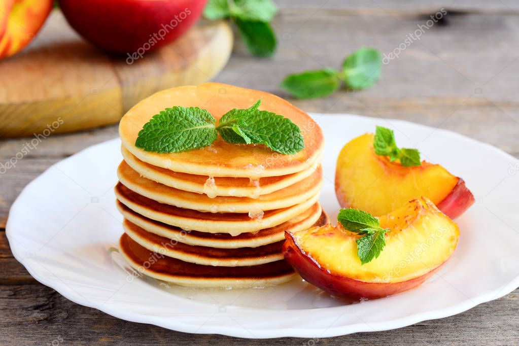 Stack of sweet pancakes with syrup and grilled nectarines slices on a serving plate. Simple pancake recipe. Tasty breakfast or brunch for kids and whole family. Closeup
