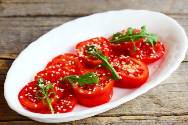 Dilimlenmiş domates, rucola, Susam salata. Eski ahşap arka plan üzerinde izole beyaz tabakta hızlı domates salatası. Dilimlenmiş Domates Salatası tarifi. Portre