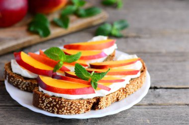 Krem peynir ve meyve sandviç fikir. Krem peynir, taze nektarin dilimleri, ceviz ve nane bir servis tabağı ve vintage ahşap bir masa ile parlak sandviç. Rustik tarzı. Portre