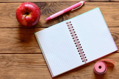 Yazılı notlar, kalem, elma, teyp santimetre ahşap bir masa üzerinde ölçüm için açık defter. Egzersiz ve diyet günlüğü metin için kopya yer ile. Zayıflama kavramı