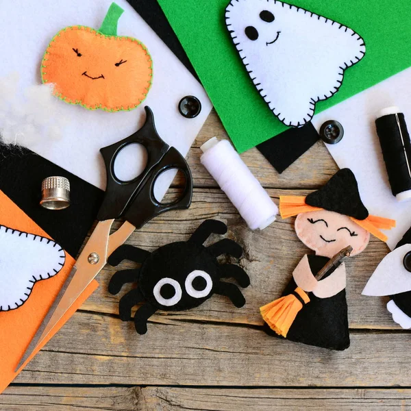 Felt toys for Halloween home decor clearance. Felt witch with broom, pumpkin head, ghost, spider. Handmade Halloween decorations. Felt sheets, scissors, threads on a wooden table. Top view. Closeup