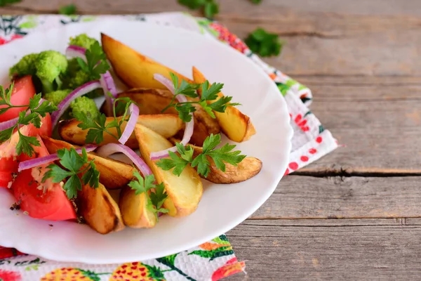 Papas fritas, brócoli cocido, tomate fresco con especias, cebolla roja, hojas de perejil en un plato blanco y en una mesa de madera vieja. Sabroso plato de verduras — Foto de Stock