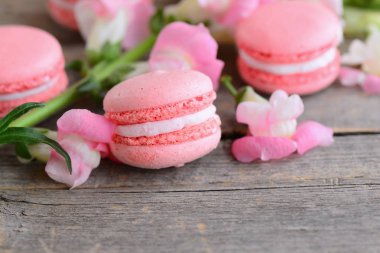 Popüler Fransız pastaları macarons. Hafif pembe macarons ve kopya alanı metin için vintage bir ahşap zemin üzerine çiçekler. Tatlılar arka plan. Portre