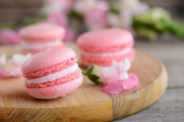Fransızca macaroons tarifleri. Hafif pembe yuvarlak macaroons ve bir ahşap tahta çiçekler. Antika ahşap arka plan. Tatlılar fotoğraf. Portre