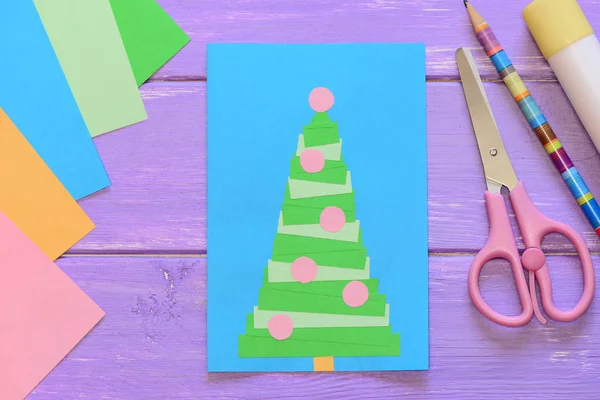 Рождественская открытка, ножницы, клеевая палка, карандаш, цветная бумага на фиолетовом деревянном фоне. Творческая поздравительная открытка с елкой. Создание простых подарков ремесла из бумаги идея для детей. Вид сверху — стоковое фото
