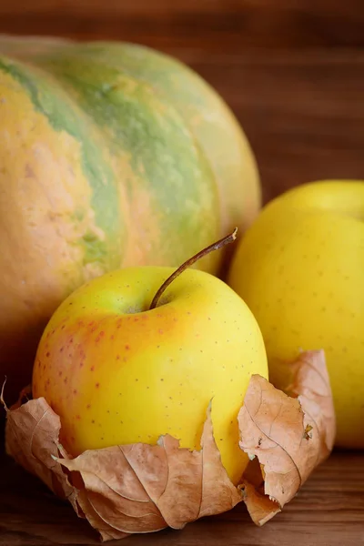 Свежие спелые яблоки и тыква на деревянном фоне. Сухой осенний лист. Вертикальное фото. Крупный план — стоковое фото